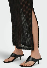 Sorte højhælede sandaler med en glat overflade, åben tå og V-formet design. Hælene er i en beskeden størrelse, der supplerer en gennemsigtig stribet beklædning.