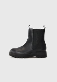 Mustad mustad Chelsea saapad, millel on ümmargune varvas, elastsed külgpaneelid, tõmbenöörid ja tükiline kummitald, millel on selgelt väljendunud kummipind.