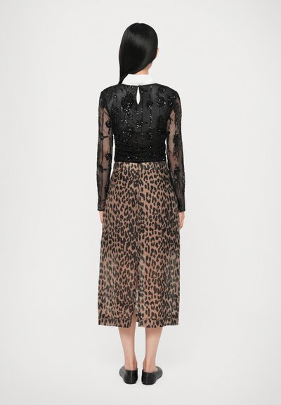 Bodice noir à sequins avec des manches longues transparentes, associé à une jupe imprimé léopard. Comprend un col blanc et un détail en trou de serrure à l'arrière. Chaussures plates noires.