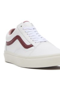 Baskets basses blanches avec une bande latérale bordeaux, des lacets blancs et une doublure intérieure rose clair, présentées sur un fond blanc.