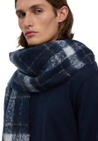 Granatowy wełniany szalik w kratę w jasnoszarym i białym odcieniu, o miękkim, teksturowanym wykończeniu i grubym, luźnym kroju.