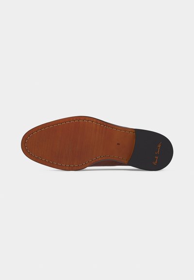 Semelle de chaussure en cuir marron avec coutures visibles et talon noir comportant le texte « Paul Smith » en cursive orange.