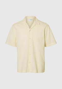 Camicetta a maniche corte di un delicato colore giallo, con un tessuto testurizzato e piccoli fori decorativi, chiusura con bottoni e un design colletto classico.