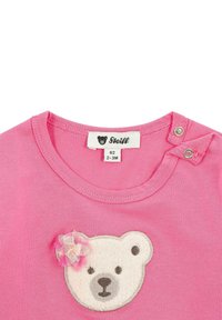 Rosa Kurzarmshirt mit einem strukturierten Bären-Applikation und einer kleinen Stoffblumenakzent. Druckknopfverschluss an der Schulter, aus Baumwollmaterial.