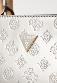 Borsa in argento metallico con motivi geometrici in rilievo, dotata di una placca logo dorata triangolare con la dicitura "GUESS U.S.A."