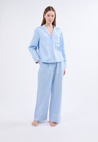 Svetle modrý bavlněný pyžamový set se zapínáním na knoflíky a kapsou, s kontrastním růžovým lemováním, doplněný širokými kalhotami.