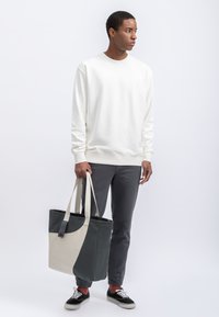 Lichte crèmekleurige sweatshirt, donkergrijze broek en een twee-kleurige schoudertas met een afgeronde vorm. Zwarte sneakers maken de outfit compleet.