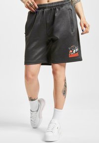 Kullgrå shorts med elastisk liv, sidelommer, og en oransje logo som sier "GUARDS." Stylet med hvite sneakers og sokker.