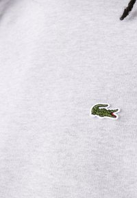 Grijze trui stof met een gestructureerd gevoel, voorzien van een klein groen geborduurd krokodil logo op de linkerkant van de borst.