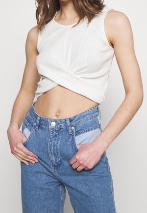 Biały prążkowany crop top z skręconym przodem, sparowany z jasnoniebieskimi dżinsami z wysokim stanem, posiadającymi kontrastowe wstawki.