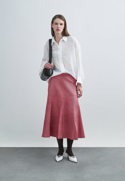 Λευκό μπλουζάκι με υφή και μακριά μανίκια, ροζ δερμάτινη φούστα A-line, μαύρες καλσόν και λευκά τακούνια με μυτερή μύτη. Μικρή καρό τσάντα ως αξεσουάρ.