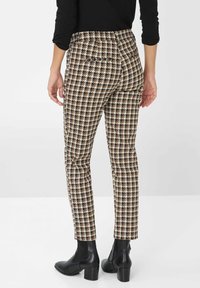 Brązowe i kremowe spodnie w wzór houndstooth o dopasowanym kroju, z dwiema tylnymi kieszeniami, noszone z czarnymi botkami za kostkę.