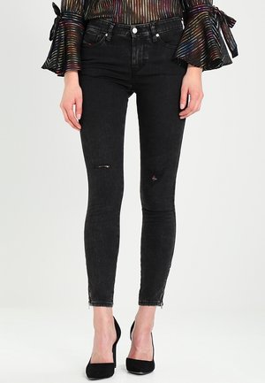 Femme portant un jean skinny noir déchiré, des talons hauts noirs et un haut à manches longues avec des rayures multicolores et des manches évasées nouées avec des nœuds.