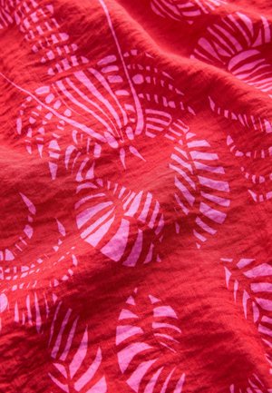 Red fabric featuring a patterned design with pink leaf motifs, showcasing a textured surface and vibrant color contrast.