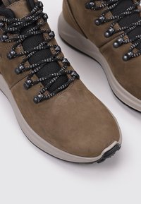 Zapatos de senderismo de ante marrón con cordones negros, que cuentan con paneles de tejido texturizado y una suela de goma de color claro para mayor agarre.