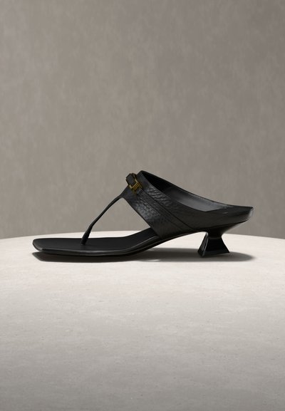 Μαύρο δερμάτινο σανδάλι με φάσα τύπου thongs, τετράγωνη μύτη, ρυθμιζόμενο χρυσό αγκράφα και χαμηλό φουσκωτό τακούνι σε ανοιχτή επιφάνεια.