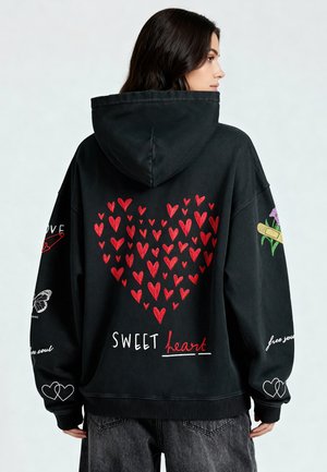 Haut à capuche noir avec un grand graphique en forme de cœur rouge et le texte blanc "SWEET heart" au dos. Présente des détails brodés, y compris un papillon.
