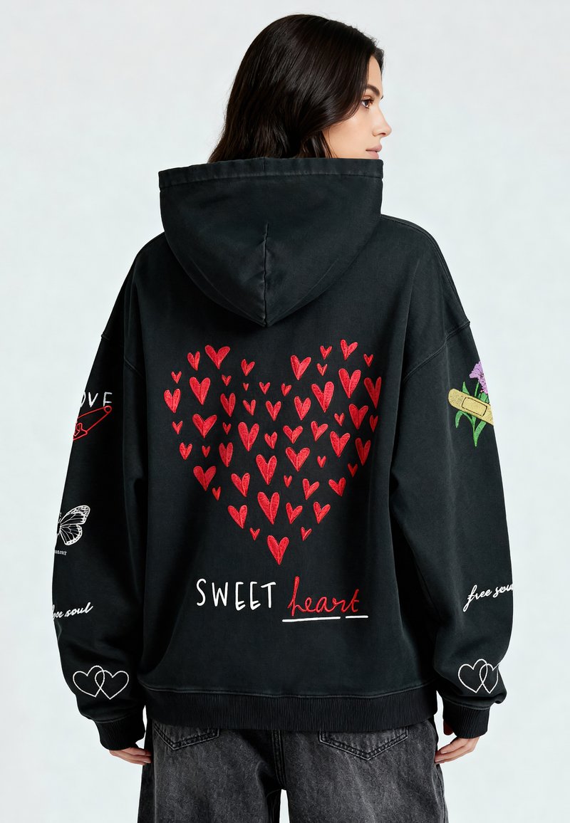 Must have kot, millel on seljal suur punane südame graafika ja valged tähed "SWEET heart". Omab tikkimisaktsente, sealhulgas liblikat.