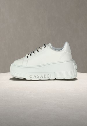 White platform sneaker with thick sole, black and white laces, and "CASADEI" embossed on the side of the sole.