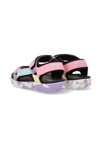 Las sandalias multicolores presentan una mezcla de tiras en rosa pastel, azul y amarillo, una base negra y una suela con un patrón de camuflaje en púrpura.