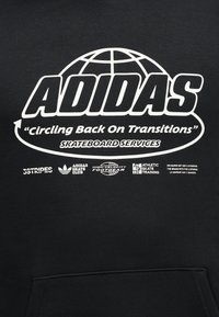 Logo Adidas avec globe et slogan « circling back on transitions » au-dessus des services skateboard et de divers logos de marques de skateboard associés sur tissu noir.