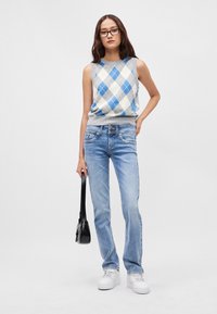 Ανοιχτό γαλάζιες τζιν με στενή γραμμή, συνδυασμένες με μια αμάνικη κορυφή σε γκρι και μπλε περσικό σχέδιο. Φοριούνται με λευκά αθλητικά παπούτσια και μαύρη τσάντα.