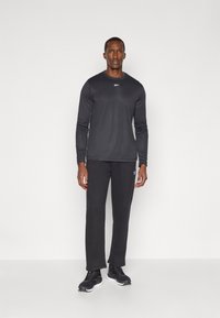 Schwarzes langärmliges Sportshirt und schwarze Hose, aus atmungsaktivem Material hergestellt. Verfügt über ein Logo auf der Brust und ein einfaches, körpernahes Design.
