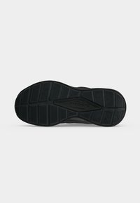 Semelle d'une chaussure Skechers noire avec des motifs sur la semelle et le logo Skechers au centre sur un fond uni.