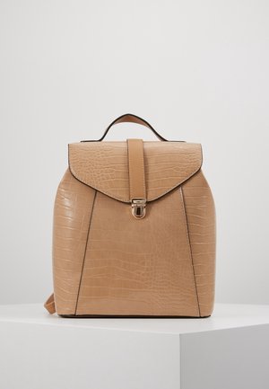 Rucksack aus braunem Kunst-Krokodilleder mit einem Tragegriff oben und einer vorderen Klappe, die mit einem goldfarbenen Verschluss gesichert ist, auf einem weißen Podest platziert.