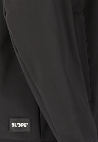 Veste à capuche noire en tissu doux et texturé, avec une étiquette logo sur le côté gauche près de l'ourlet.