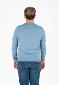 Lichtblauwe gebreide trui met een ronde halslijn en lange mouwen. Heeft ribgebreide boorden en een zoom, met een klein logoaccent aan de achterkant.