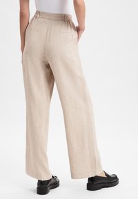 Beige, wide-leg pants made of a textured fabric. Features a high waistband, back pockets, and are paired with black shoes.