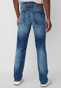 Jeans de mezclilla azul para hombre con un diseño desgastado, que cuentan con dos bolsillos traseros, un parche de cuero marrón y un corte recto.