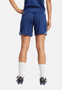 Blaue sportliche Shorts aus leichtem Material, mit einem bequemen Schnitt, seitlichen Details und einer glatten Textur. Getragen mit weißen Socken und Fußballschuhen.