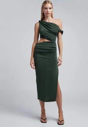Robe midi verte asymétrique avec un design torsadé sur le corsage, texture froncée et une fente haute sur la cuisse, présentant une silhouette ajustée.