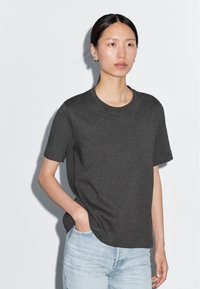 T-shirt grigio scuro a maniche corte in cotone, con collo rotondo e vestibilità comoda, abbinato a jeans in denim azzurro chiaro.