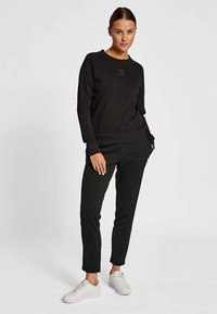 Svart sweatshirt med rund hals och långa ärmar, kombinerad med svarta avsmalnande byxor. Har subtil textur och vita sneakers.