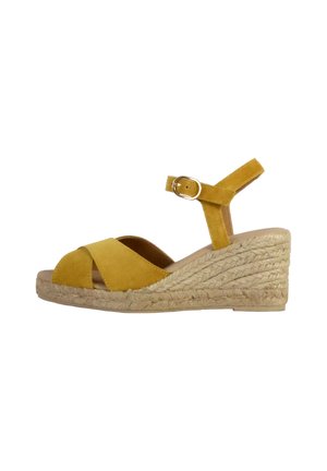 Yellow suede wedge sandal with cross-over straps and adjustable ankle strap, featuring a woven jute sole for added texture.