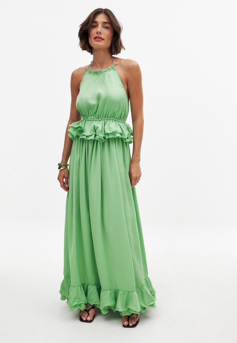 Vihreä maxi-mekko, joka on valmistettu sileästä satiinista, jossa on röyhelövyötärö ja -haalari. Olkaimeton malli, jossa on kerrottu kaula-aukko ja virtaava kangas.