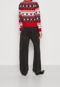 Pull de couleur rouge et bleue à motifs de flocons de neige et de rennes, associé à un jean noir à jambes larges et des chaussures noires. Le pull possède des poignets côtelés.