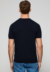 Marinblå kort ärmad tröja i ett slätt stickat tyg med rund halsringning och ribbat kant, bärs tillsammans med blå denimjeans.