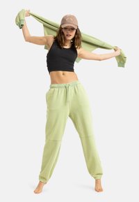 Lys grønne, løstsiddende sweatpants med elastisk talje. Sort, tætsiddende crop top og en lys grøn sweatshirt draperet over skuldrene.