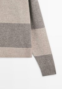 Pullover rayé gris et beige avec une texture douce. Présente des poignets et un ourlet côtelés, mettant en valeur des lignes horizontales épaisses alternées.
