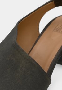 Μαύρο σουέντ παπούτσι με ανοιχτή πίσω πλευρά και φαρδιά μπροστινή λωρίδα. Η εσωτερική επιφάνεια διαθέτει ομαλή ταμπά επένδυση. Επίπεδη σόλα με ελαφρύ υφή.