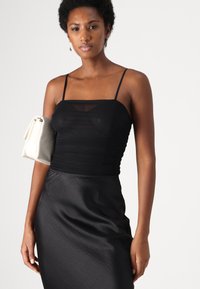 Débardeur noir froncé avec des fines bretelles, associé à une jupe noire élégante. Complété par un petit sac à main blanc. Texture lisse.