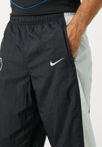 Black and light gray athletic pants with a textured finish, featuring an elastic waistband and a small white logo on the front.