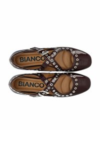 Bruna lackskor med ett utskuret mönster, dekorativa metalöglor och korsade remmar med spänne.