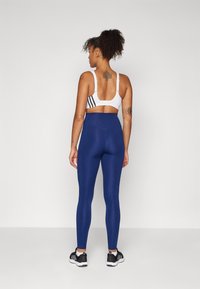 Trenings-BH med hvit bunn og svarte striper; høytiddde blå leggings; begge laget av elastisk stoff; treningssko med svart og hvite detaljer.