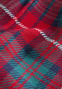 Tela de tartán rojo y verde con un patrón de diamantes, detalles en azul marino y líneas blancas, que muestra una suave textura de punto.