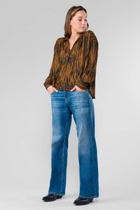 Losse, lange mouw blouse in zwart met een roestkleurig golfpatroon; gecombineerd met lichtblauwe, uitlopende denim jeans en zwarte enkellaarsjes.